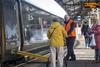 Staff member assisting passenger with mobility aid onto train with ramp deployed at a train station