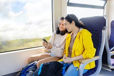 Two woman friends travelling by train looking at cell phone