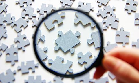 Hand,With,Magnifying,Glass,And,Puzzle,Isolated,On,White,Background