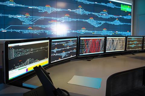 Operators at desks in a railway control room facing a wall of screens